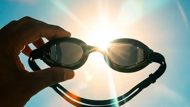 Dark mirrored swimming goggles held up directly against a bright, glaring mid-day sun