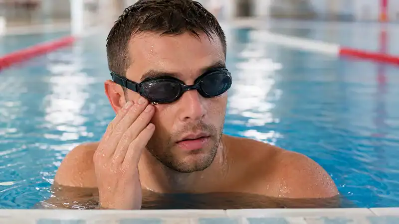 Swimmer in goggles surfacing from pool water with an irritated eye after a hard session