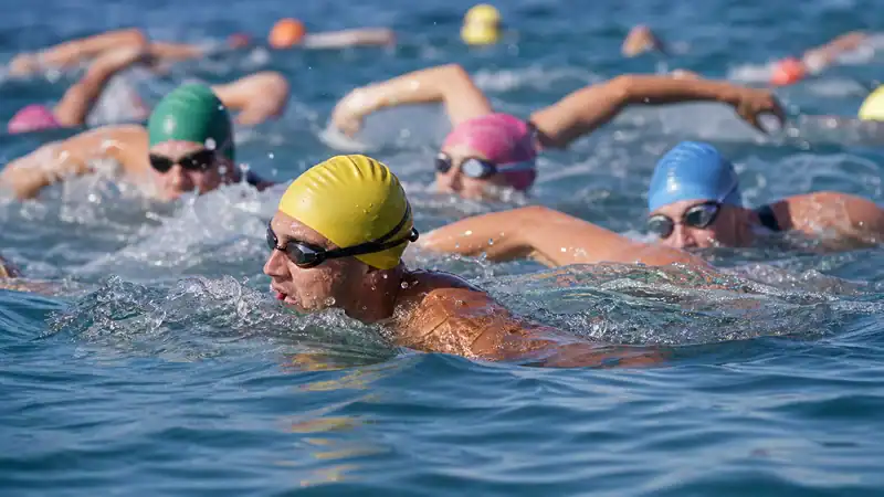 Open-water swimmers in close contact wearing caps and goggles at a race start
