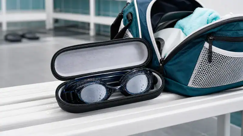 Swim goggles stored in a hard protective case beside a pool bag